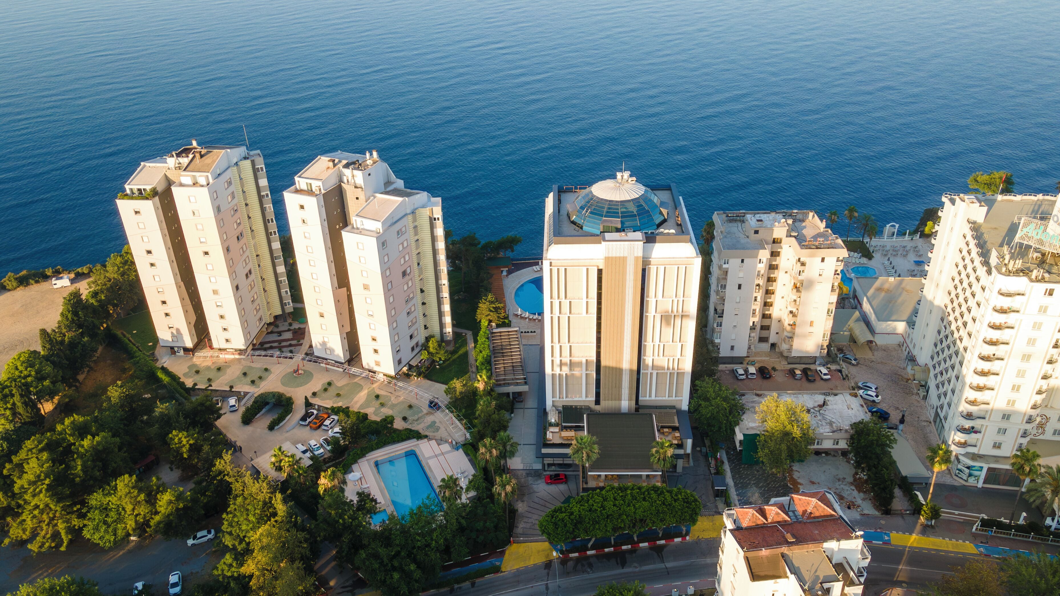 A high-rise hotel with multiple floors, a swimming pool, and a beach area.