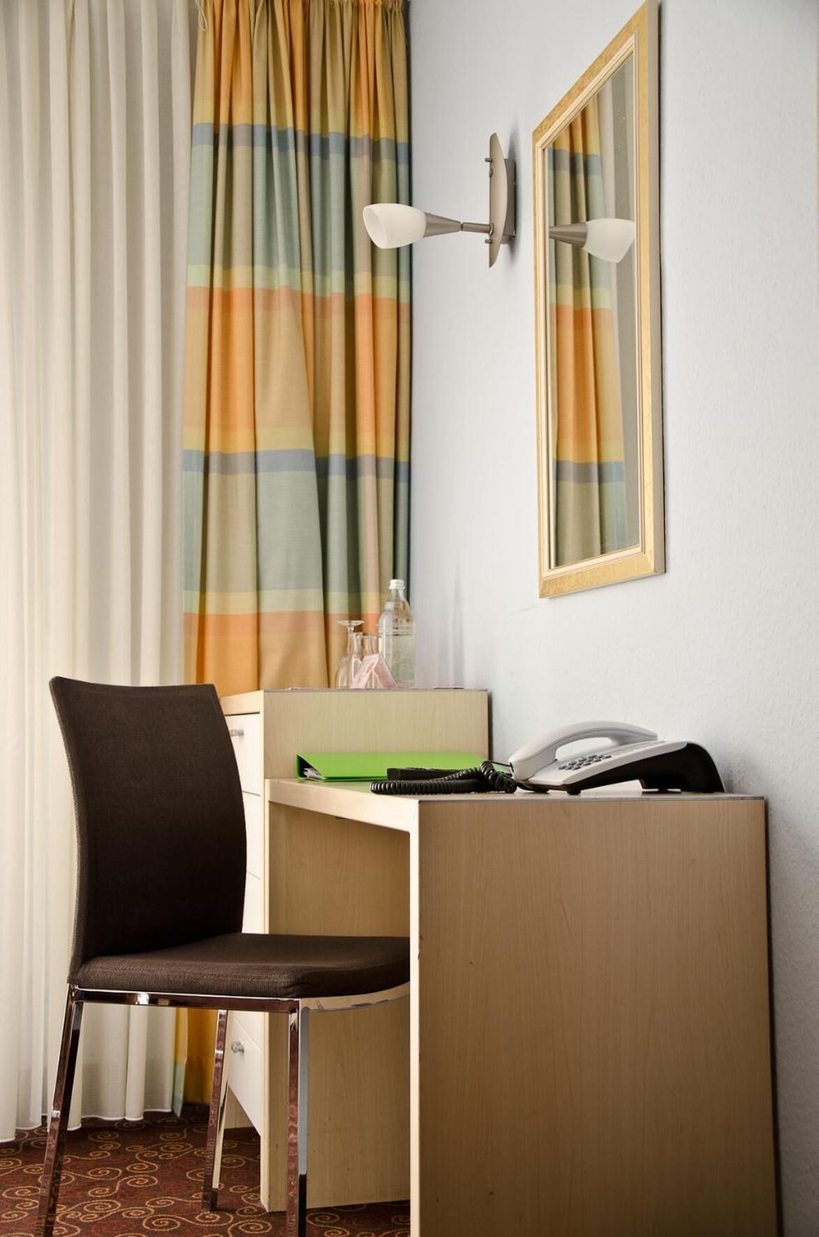 A hotel room with a desk, chair, telephone, and a mirror.