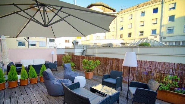An outdoor patio with wicker furniture, potted plants, and a large umbrella. - Hotel Rheinland (Bonn)