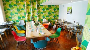 A dining area with a long table set for multiple people, surrounded by colorful chairs. - Hotel Rheinland (Bonn)