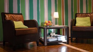 A room with two wicker armchairs, a small side table with a lamp and a fruit bowl, and a striped wall. - Hotel Rheinland (Bonn)