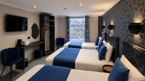 A hotel room with two beds, a TV, a desk, and a view of the city. - Mentone Hotel (London)