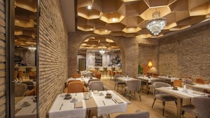 A restaurant with brick walls, hexagonal ceiling patterns, and chandeliers. Tables are set with white tablecloths and silverware. - Condotti Palace (Rome)