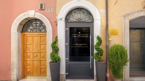 A building facade with a central entrance featuring a dark door with a sign reading "CONDOTTI PALACE". - Condotti Palace (Rome)