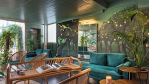 A room with a green sofa, wicker chairs, a small table with a candle, and a mural of trees. - Condotti Palace (Rome)