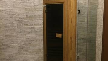 En-suite bathroom features a glass shower enclosure, a small table with a remote control and a card, and a round clock on the wall.