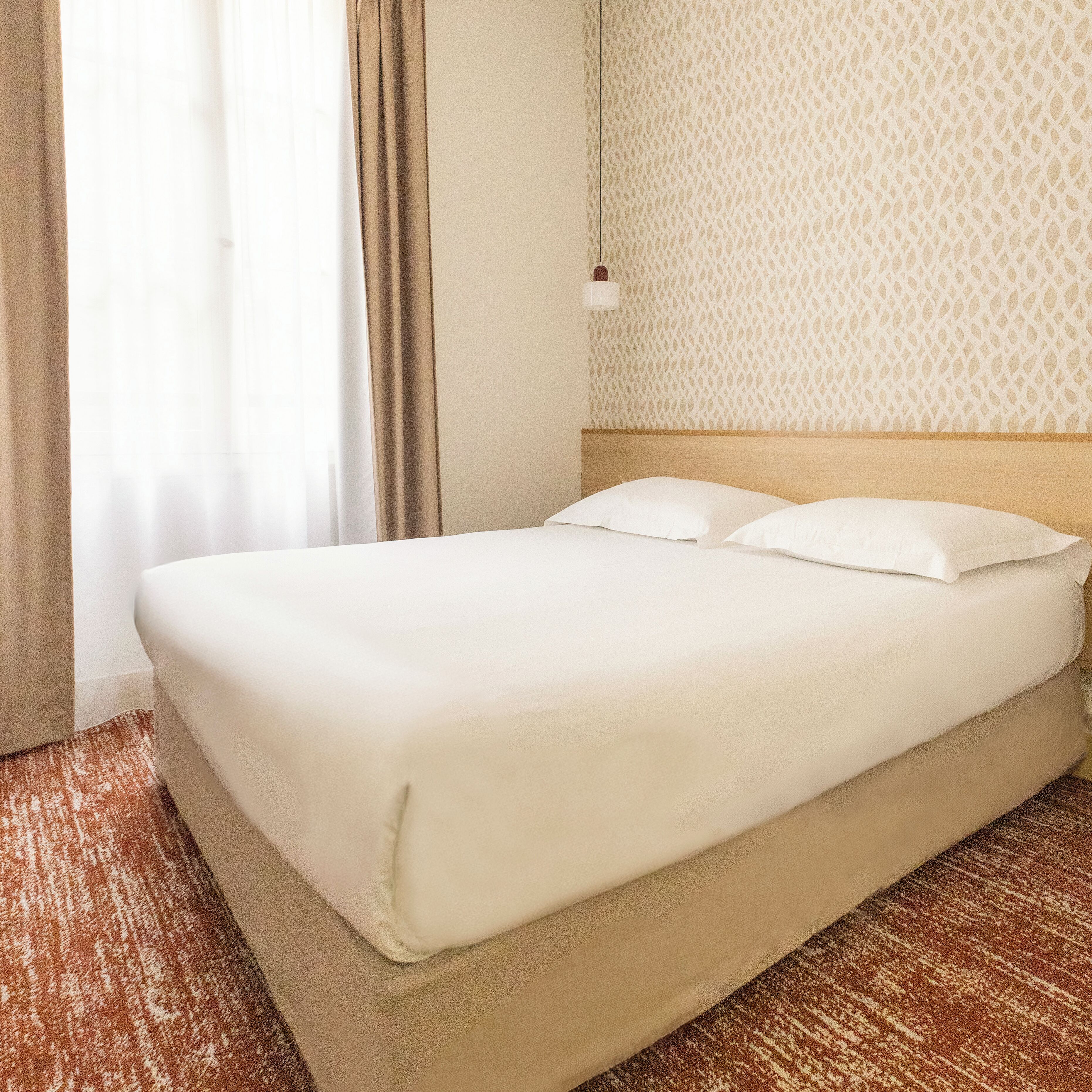 Un lit bien fait, avec du linge de lit blanc, dans une chambre d’hôtel.