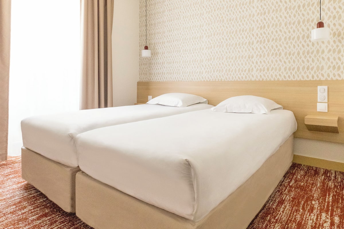 Una habitación de hotel con una cama doble, una mesita de noche, una lámpara y papel tapiz estampado.