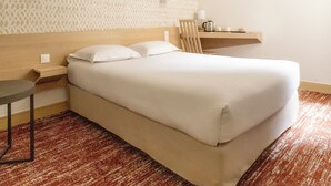 Een net opgemaakt bed met witte lakens, een houten hoofdbord, een klein nachtkastje met een lamp en een behang met patroon.