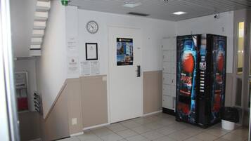 A hallway with a clock, a door, vending machines, and a trash bin.