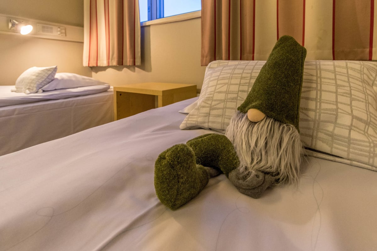 A hotel room with two beds, one with a green gnome decoration, and a nightstand with a lamp.