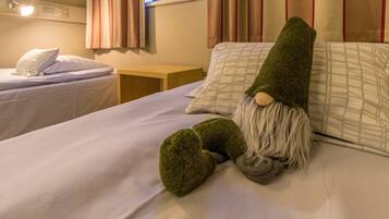 Una camera d'albergo con due letti, uno decorato con un gnomo verde e un comodino con una lampada.