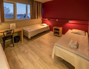 A hotel room with two beds, a desk, a chair, a small shelf, and a view of the outside.