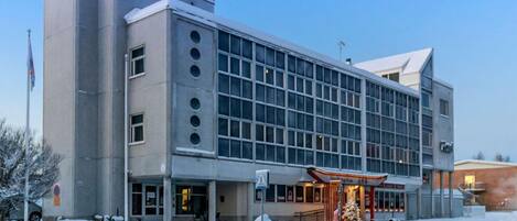 Een modern hotel met een grote glazen gevel, een opvallende ingang met een rode luifel, en een met sneeuw bedekte omgeving.
