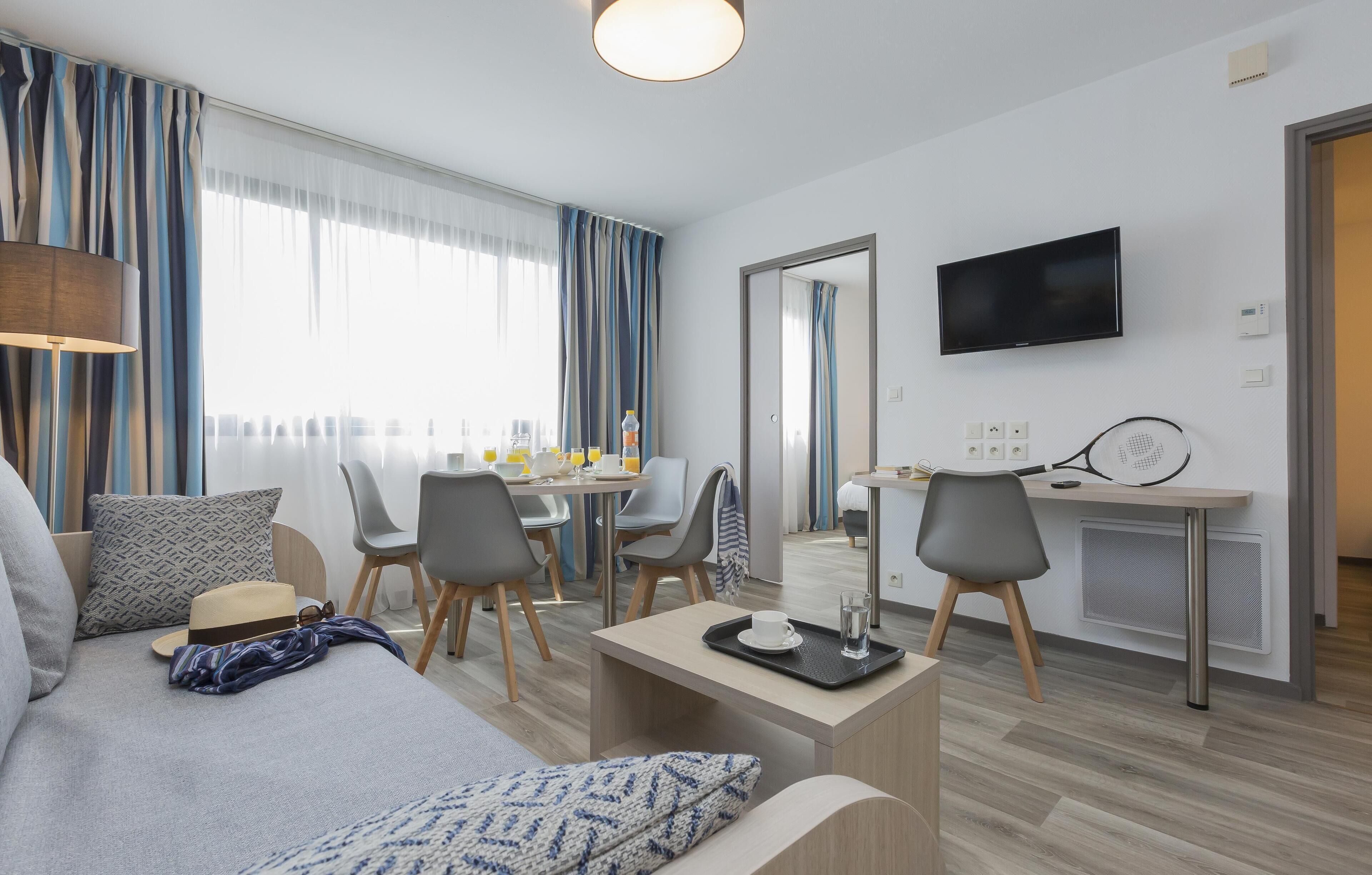 Ein modernes Hotelzimmer mit einer Sitzecke, einem Esstisch und einem Fernseher.