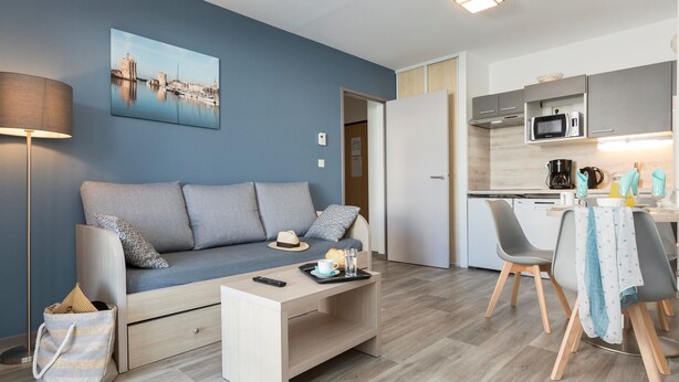 A modern living room with a sofa, a coffee table, and a dining area with chairs and a table. - Résidence Hôtelière Odalys l'Archipel (La Rochelle)