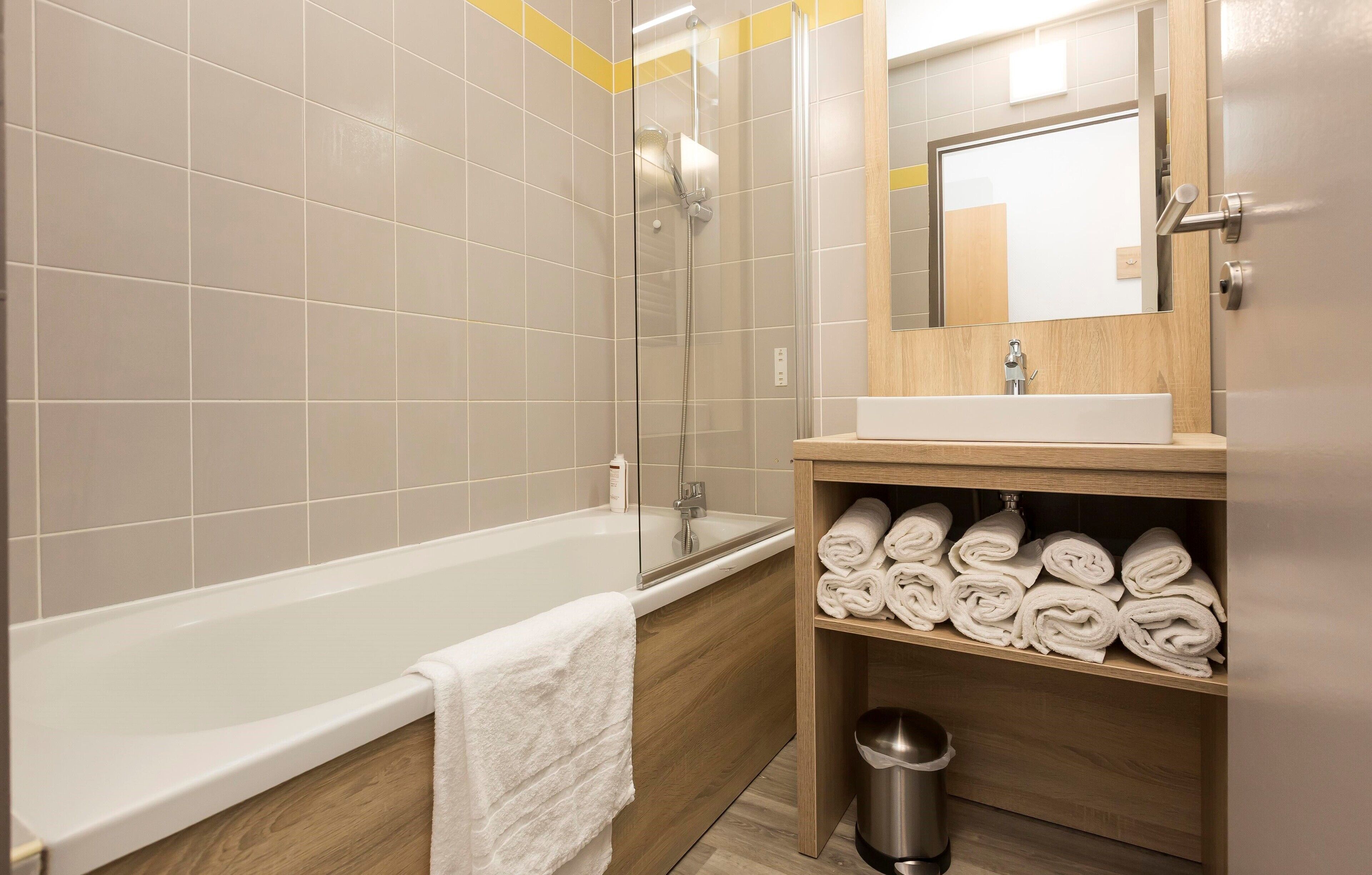 A modern bathroom with a bathtub, a glass-enclosed shower, and a wooden vanity with towels.