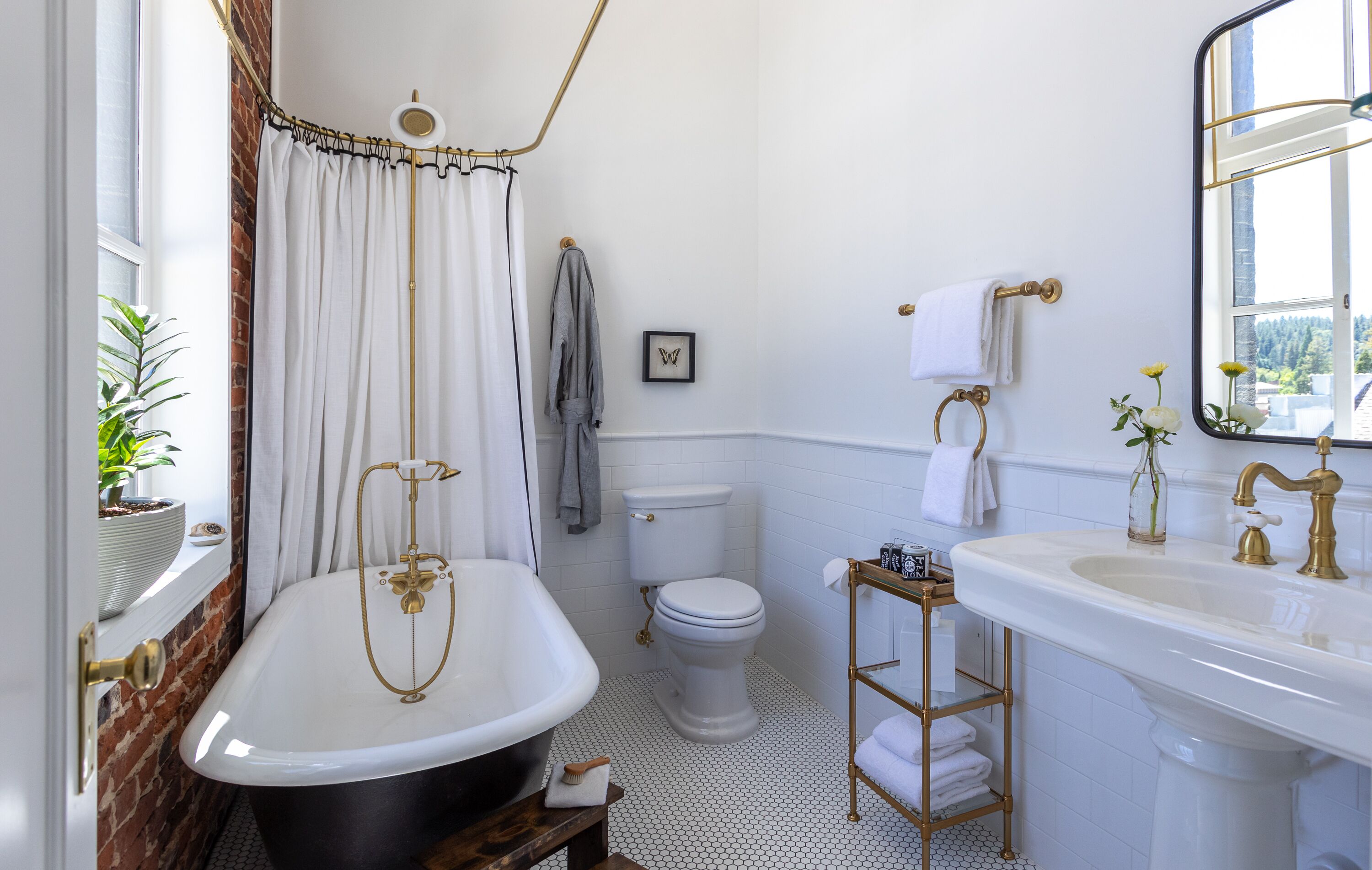 Een badkamer met een vrijstaand bad, een toilet, een wastafel met gouden kraan en een spiegel boven de wastafel.
