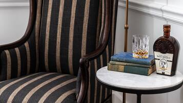 Un sillón a rayas, una mesita redonda pequeña con una botella y libros, y una lámpara de pie.