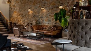A cozy living room with a stone wall, leather sofas, a coffee table, and a staircase. - Holbrooke Hotel (Grass Valley)