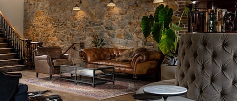 A cozy living room with a stone wall, leather sofas, a coffee table, and a staircase.