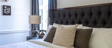 A neatly made bed with a tufted headboard, a bedside lamp, and a framed picture on the wall.