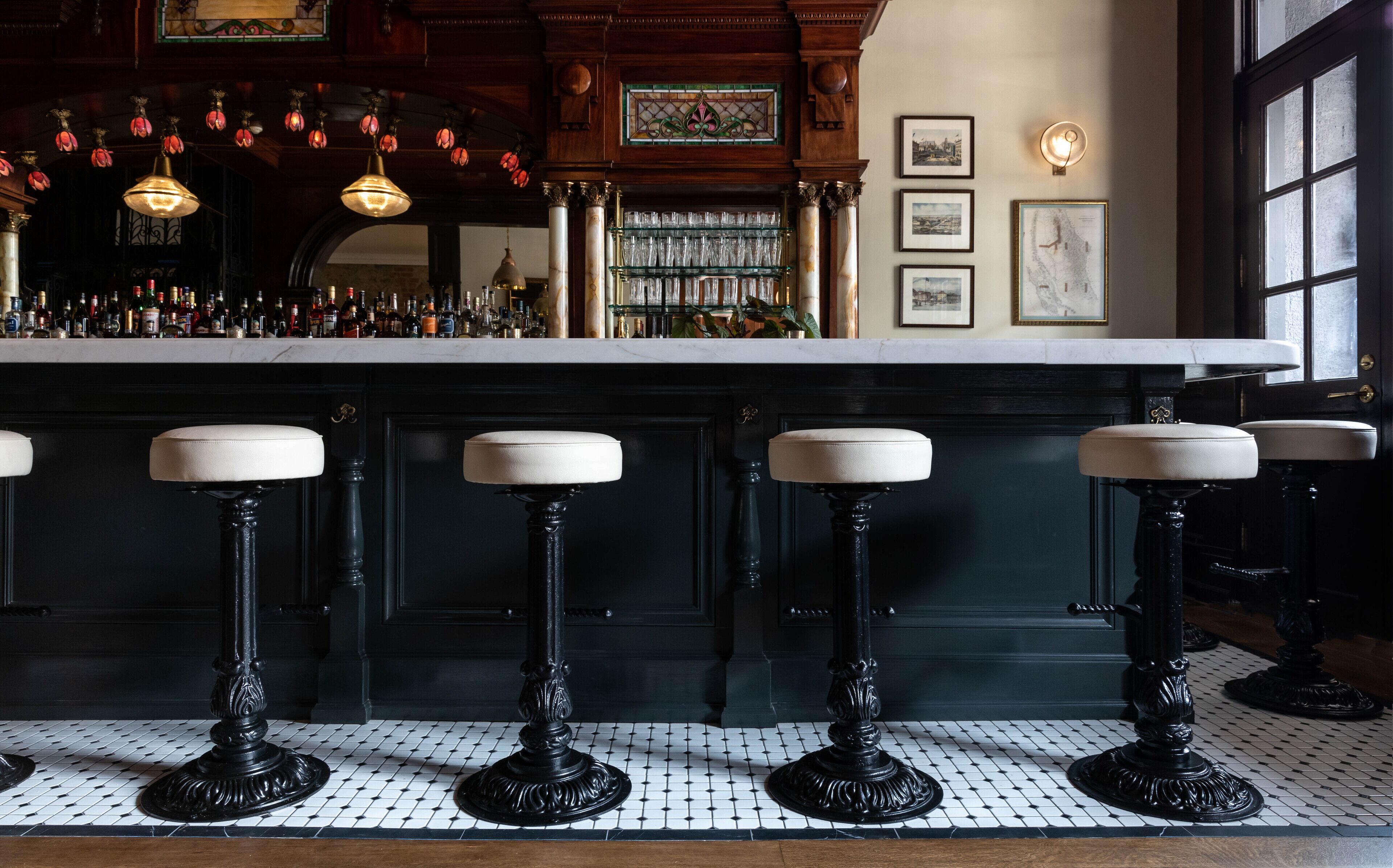 A bar area with black stools, a tiled floor, and a bar counter with bottles.