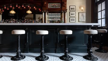 A bar area with black stools, a tiled floor, and a bar counter with bottles.