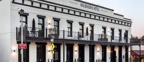 A two-story building with the sign "Holbrook Hotel, Valley." It features a balcony with black railings and potted plants.