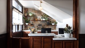 A kitchen with wooden cabinets, a marble countertop, a stone wall, and a hanging light fixture. - Holbrooke Hotel (Grass Valley)