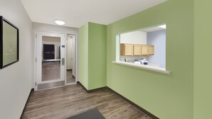 A hallway with a green wall, a wooden floor, a mirror, and a reception desk. - WoodSpring Suites Des Moines Pleasant Hill (Pleasant Hill)