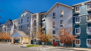 A multi-story hotel with a sign reading "Woodspring Suites." It features a covered entrance, multiple windows, and a parking lot. - WoodSpring Suites Des Moines Pleasant Hill (Pleasant Hill)