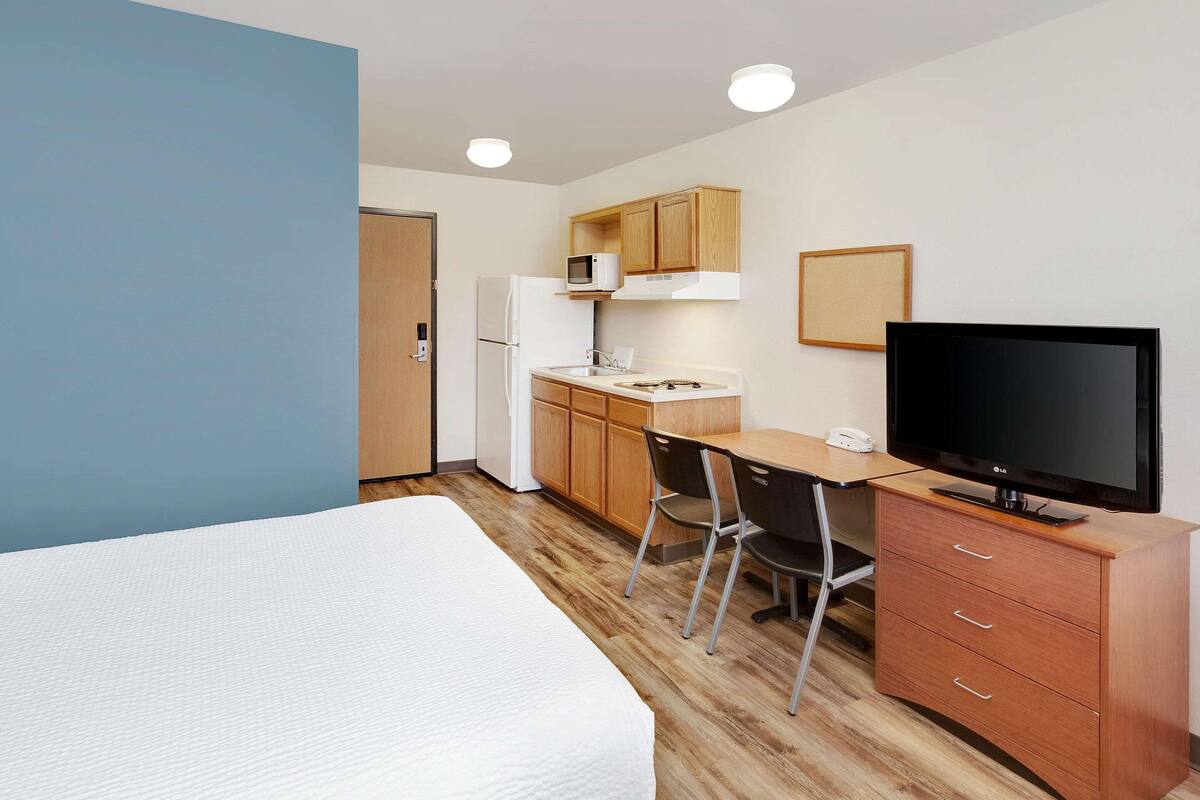 Une chambre d’hôtel compacte comprenant un lit, une kitchenette, un bureau avec une chaise, une télévision et une armoire.