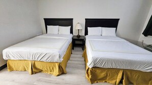 Habitación de hotel con dos camas, cada una con ropa blanca y cubrecolchones dorados. Un mesita de noche entre las camas tiene una lámpara encima.