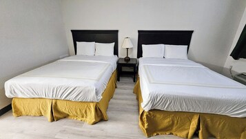 Habitación de hotel con dos camas, cada una con ropa blanca y cubrecolchones dorados. Un mesita de noche entre las camas tiene una lámpara encima.