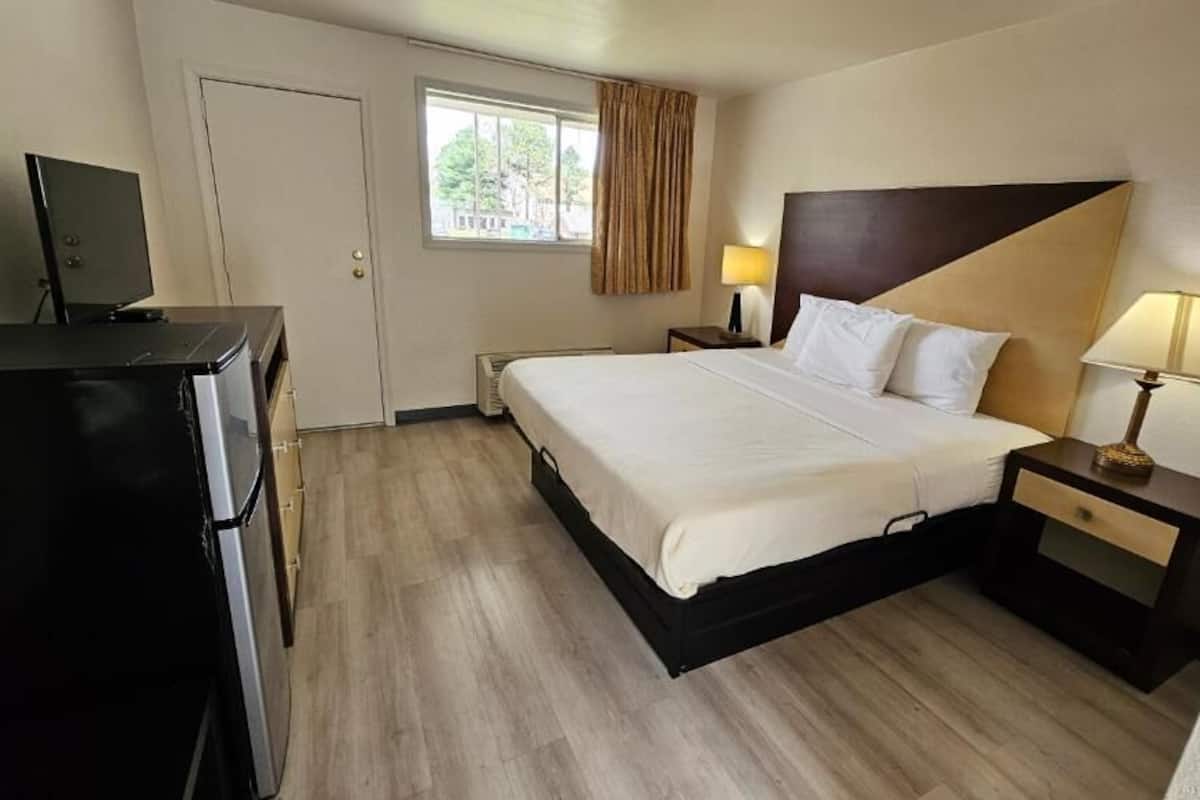 A hotel room with a bed, bedside tables, a TV, and a window with curtains.