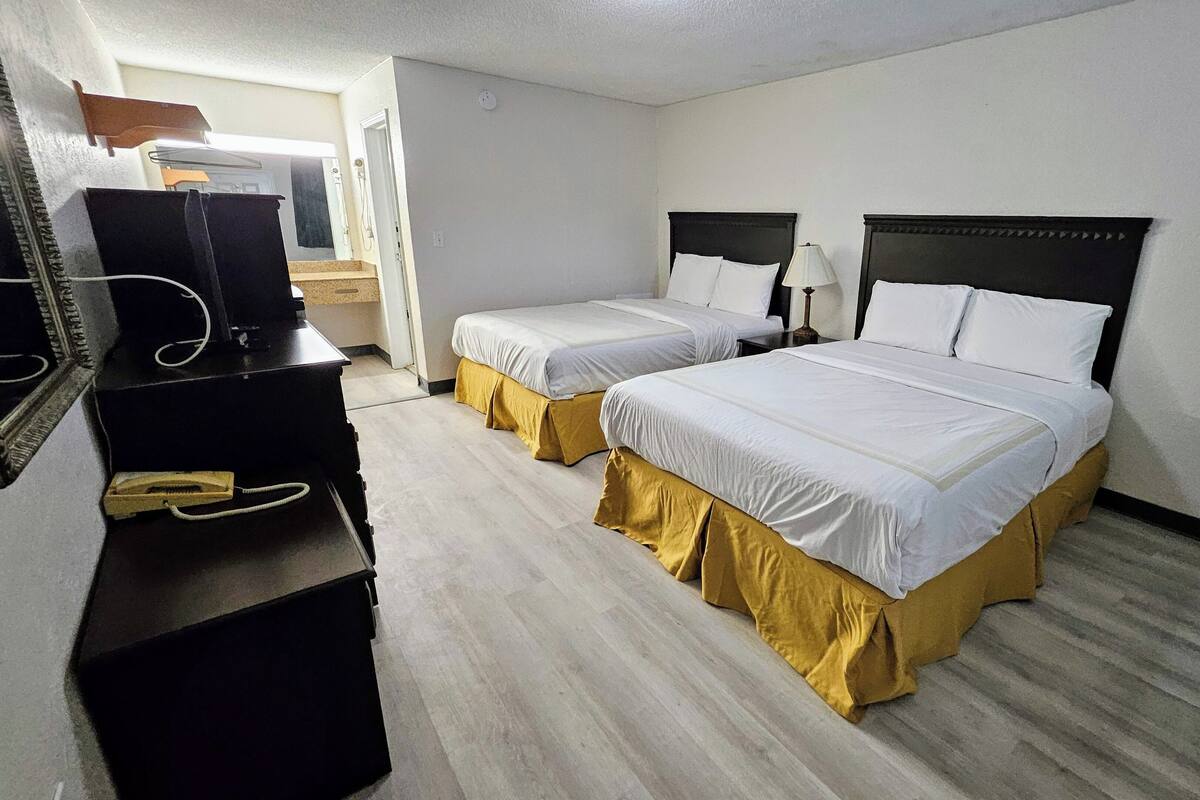 A hotel room with two beds, a desk, a chair, a lamp, and a television.