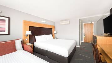Habitación de hotel con una cama grande, un escritorio, una silla, un televisor y una puerta que da a otra habitación.
