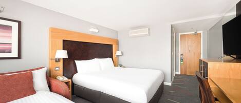 Habitación de hotel con una cama grande, un escritorio, una silla, un televisor y una puerta que da a otra habitación.