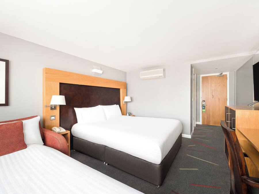 Habitación de hotel con una cama grande, un escritorio, una silla, un televisor y una puerta que da a otra habitación.