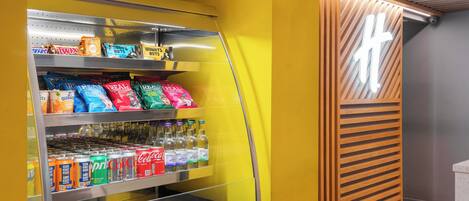 Un distributeur automatique de collations et de boissons, notamment des barres Twix, des biscuits Oreo et des chips Pringles, avec un intérieur jaune et en bois.