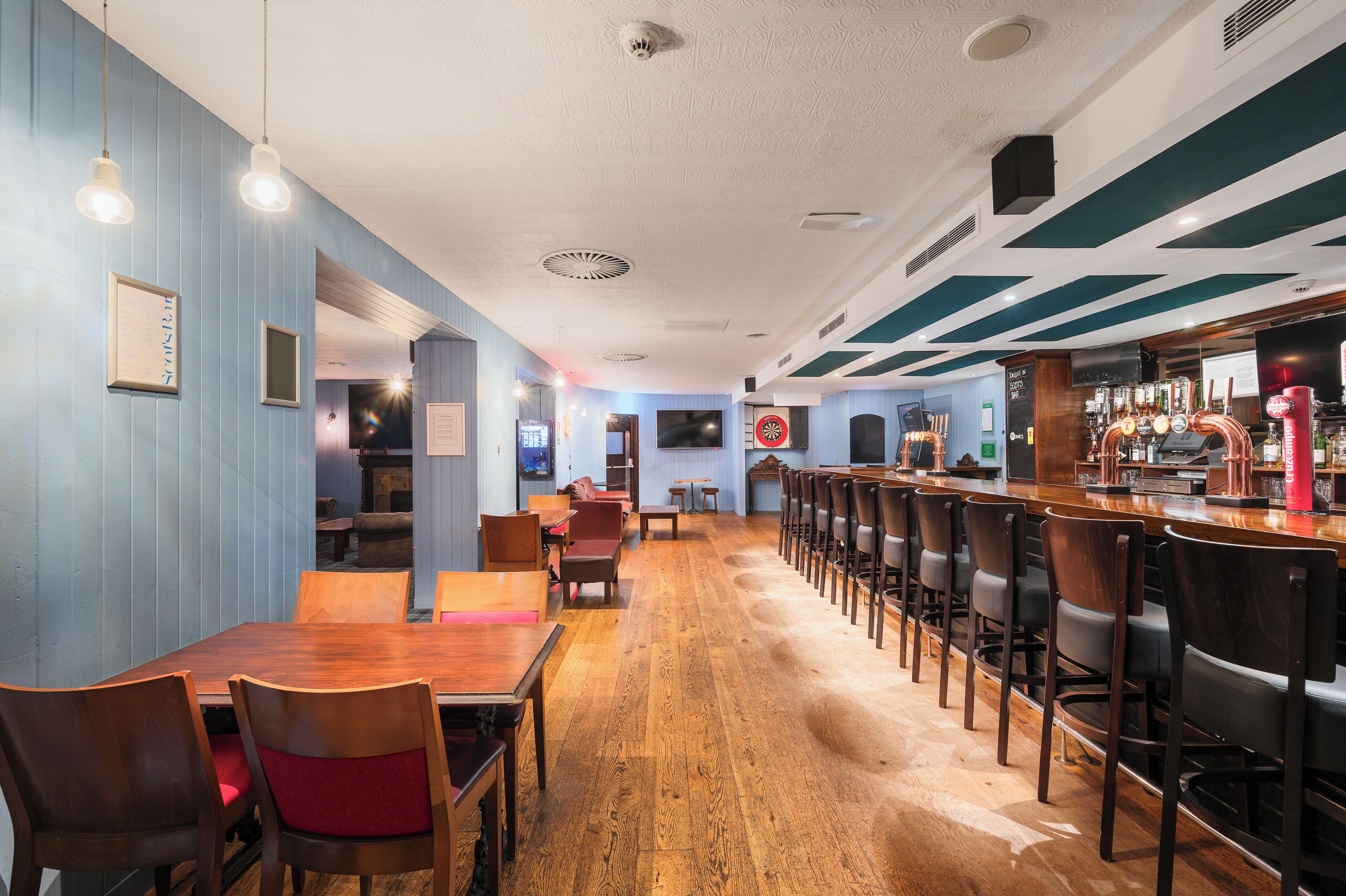 A restaurant with wooden tables and chairs, a bar area with stools, and a blue and white color scheme.
