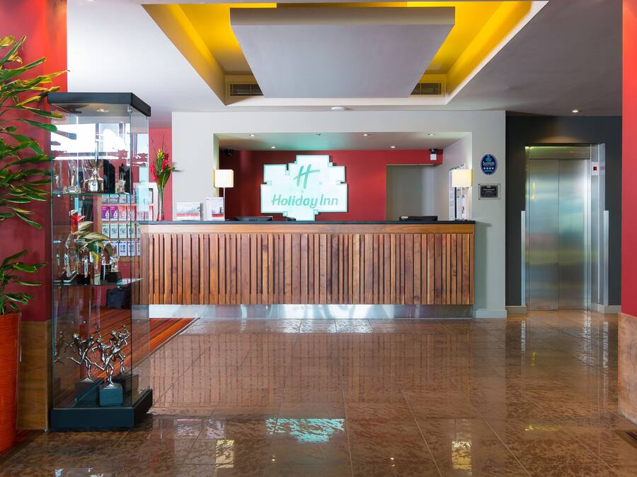 Ein Empfangsbereich eines Holiday Inn mit einem hölzernen Empfangstresen, einer Vitrine mit Auszeichnungen und einer Farbgestaltung in Rot und Gelb.