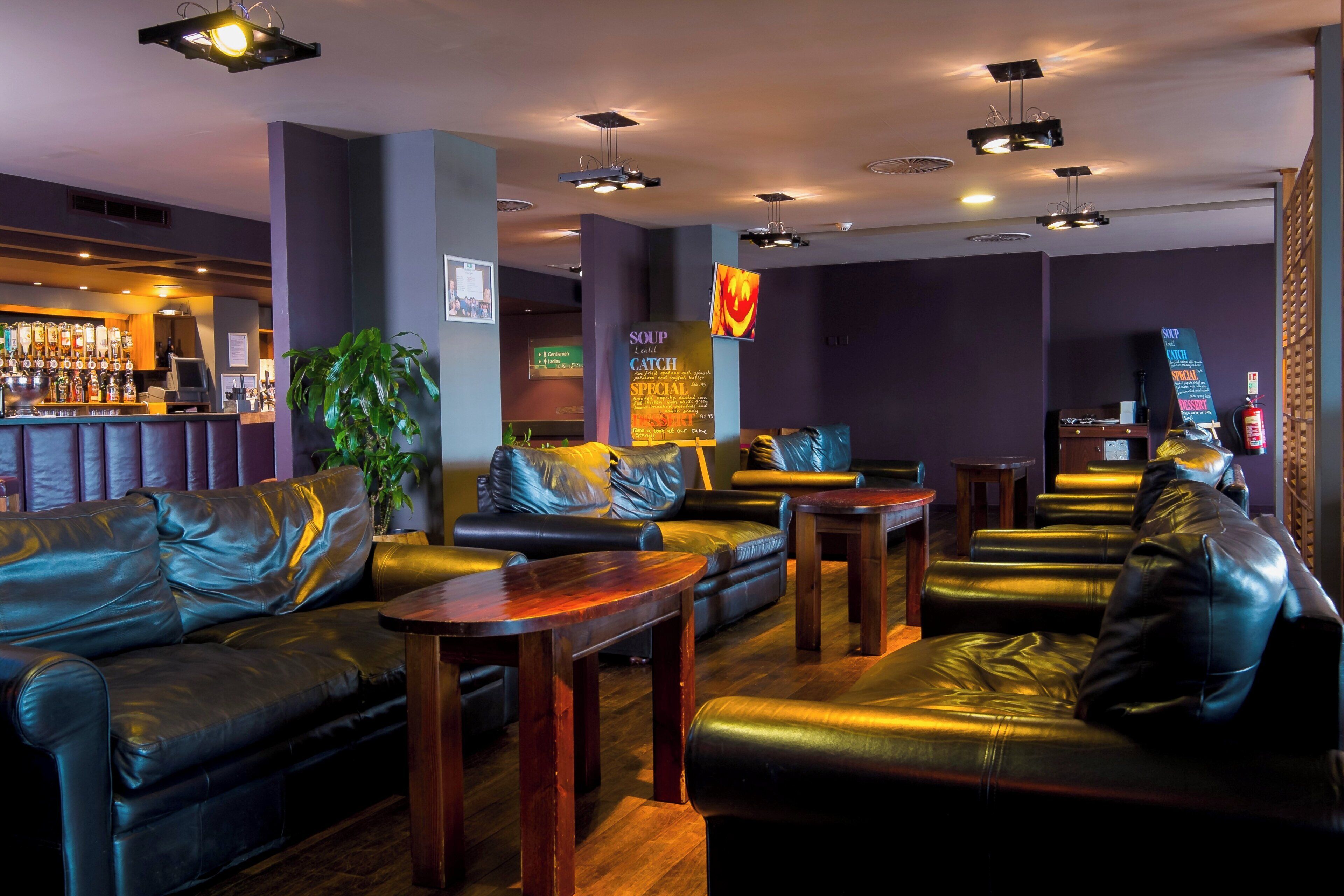 A bar area with leather seating, a bar counter with bottles, and a menu board.