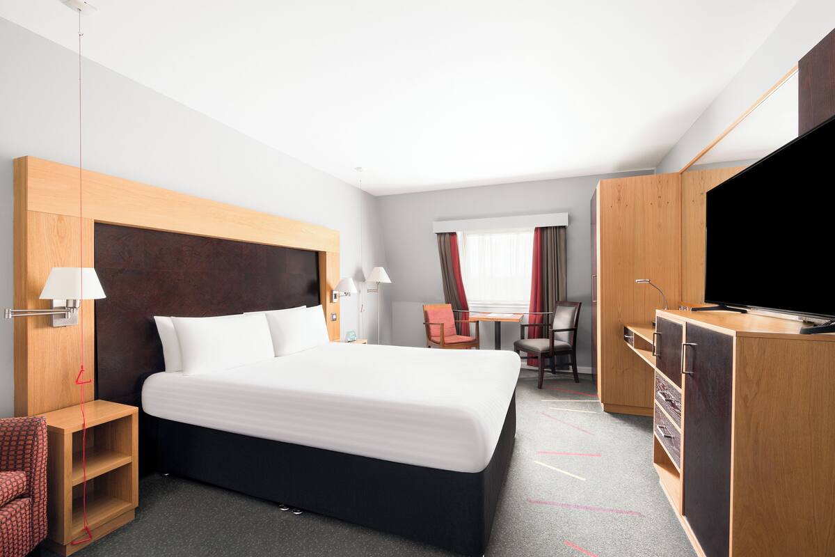 A hotel room with a large bed, a desk, a TV, and a wardrobe.