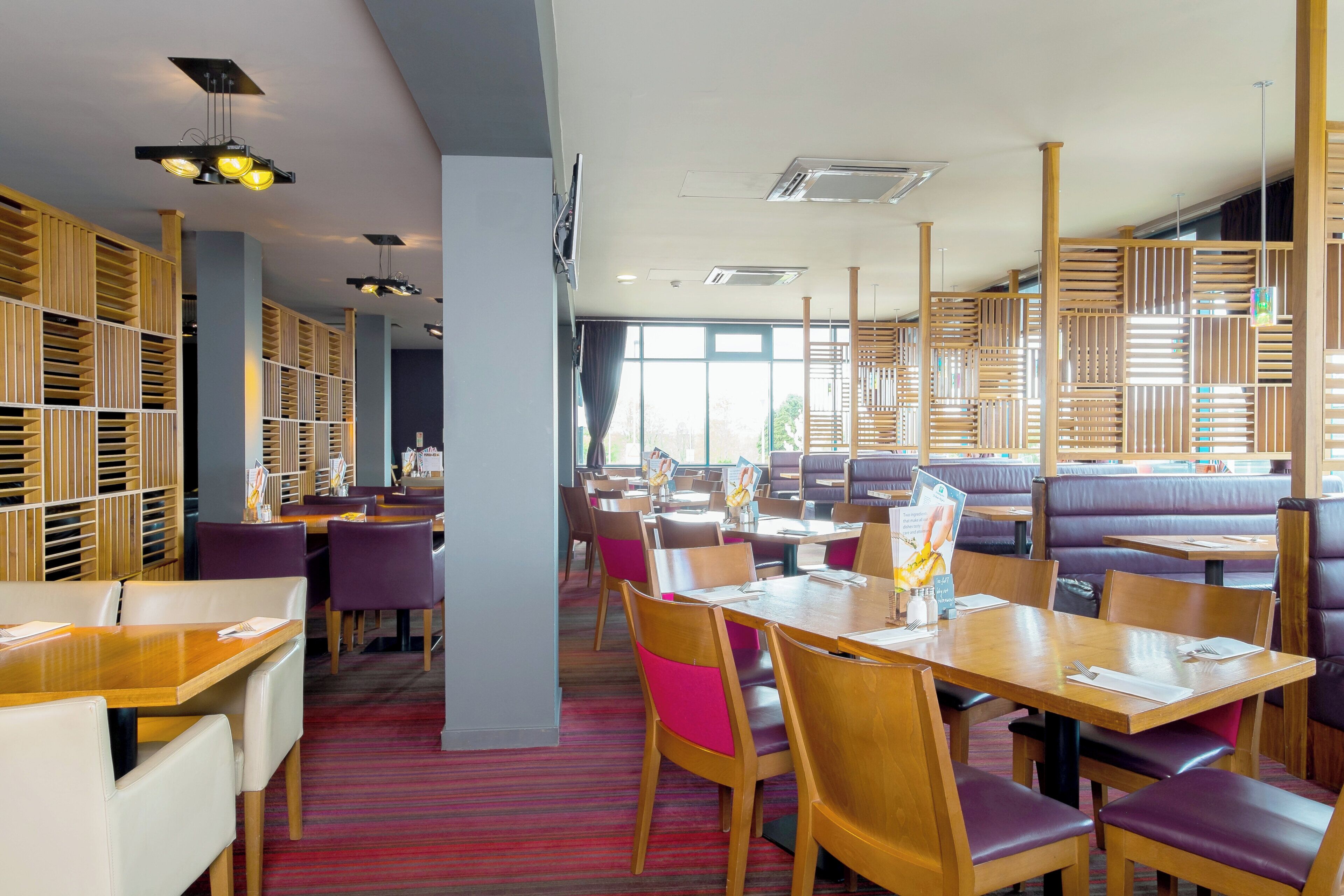 Un restaurante con muebles de madera, mesas y sillas, y vistas al exterior a través de amplios ventanales.