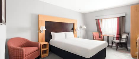Habitación de hotel con una cama grande, un sillón rojo, una mesita de noche de madera, un escritorio con silla y un armario.