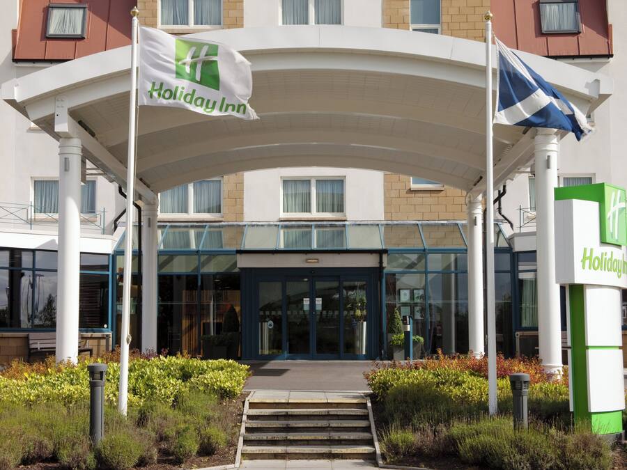 L’entrée d’un hôtel Holiday Inn, avec un passage couvert, des portes en verre et un drapeau.