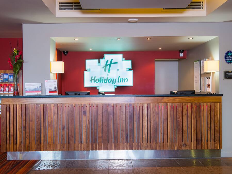 A reception desk with a wooden panel design, a 'Holiday Inn' sign, and a reception area with a red wall and a 'Scottish Hotel' sign.