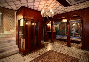 A grand lobby with a large chandelier, ornate wooden doors, and a patterned floor.